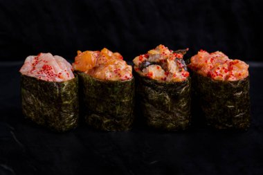 Warm rolls with tuna, salmon, perch, eel, tobiko caviar, nori, rice, cucumber on a black background