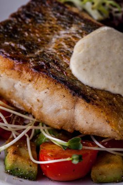 Fried sebasse with mashed potatoes, frize salad, young shoots, cherry tomatoes on a white round plate. Vertical orientation 