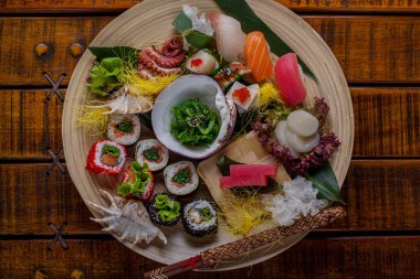 Meat of tuna, shrimp, squid, octopus, salmon, eel, perch with lime, chuka avocado, sesame seeds, carrots, sushi, salmon caviar, cheese, shell, salad and cabbage on banana leaves in a plate on a wooden table and chopsticks