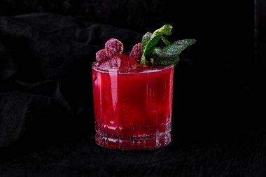 Buzlu kokteyl, ahududu ve nane şekeri. Koyu renk kumaş arka planda, ahşap bir masada duruyor.