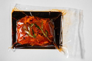 Vacuum packed raw marinated meat with peppercorns and rosemary on a white background
