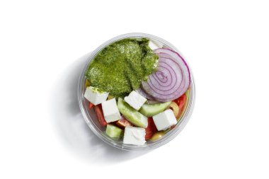 Mozzarella with cucumbers, tomatoes, onions and pesto sauce in a plastic container on a white plate