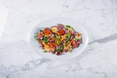 Salad with meat, tomatoes, arugula, chips and sauce in a plate on a marble background