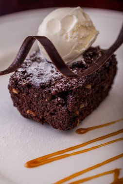 Çikolatalı kek, çikolata parçacıklı, bir kepçe dondurma ve beyaz tabakta karamel. Dikey yönelim