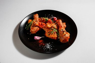 Raw marinated chicken legs with peppercorns, paprika, salt, rosemary and garlic in a plate on a white background