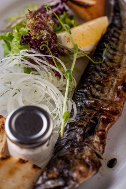 Fried mackerel, with potatoes, onion rings, lemon wedge, young shoots, salad and sauce. Vertical orientation