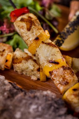 Fish fillet on a skewer, kebab lula with white sauce and parsley, a slice of lemon and sesame seeds on a wooden plate with a glass of white wine. Vertical orientation 