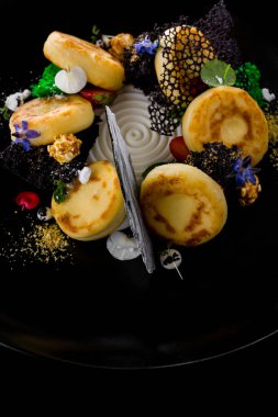 Ekşi kremalı, naneli, mikro yeşil, böğürtlenli, ahududulu ve yenilebilir yapraklı peynirli kekler. Siyah bir levhada yatıyorlar. Siyah bir arkaplanda.