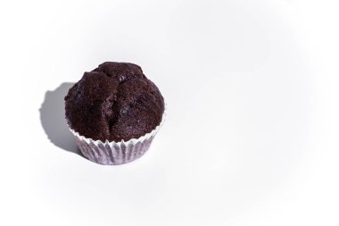 Chocolate cupcake in paper wrapper on white chair against white wooden wall background