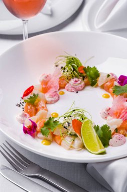 Yanında Japon mayonezli tobiko havyarı, kişniş yaprağı, lahana turşusu, soğan mikroyeşil, acı biber dilimleri ve bir damla mango sosu var. Yemek beyaz, derin, yuvarlak bir tabakta. Tabak beyaz şeritte.