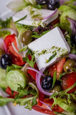 Salad with cheese, olives, onions, tomatoes, lettuce, arugula and sauce in a plate on a light table with a glass of wine.