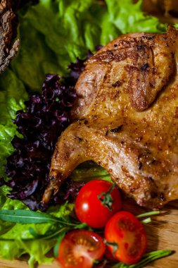 Kirazlı domates ve marullu tavuk tabakası yanında da domates soslu sos kabı var. Arkada bir bardak bira var. Tahta bir tahtanın üzerinde yiyecek ve bira standı. Etrafta barbekü kütükleri var..