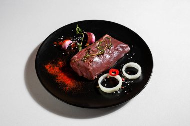 Raw beef meat with peppercorns, onions, paprika, salt, thyme and garlic in a plate on a white background