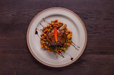 Kemiğin üzerinde kuzu kuzu eti, kekik, biber ve nohut ile ahşap bir arka planda bir tabak. Yatay yönelim