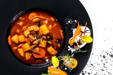 Soup with carrots, mung bean salad, sprouts, flower petals, kumquat, sauce, beans, potatoes and peppers in a plate on a white background