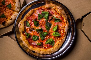 Pizza with prosciutto cheese, basil, bacon, pepper and sauce on a plate on the table