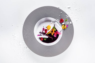 Meringue plates with sorbet, raspberries, mint, kumquat, lace chips, flower petals and powdered sugar in a plate that stands on a white background