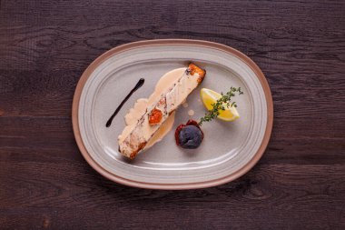 Sos soslu kızarmış somon bifteği, kekik, limon ve domates oval tabakta ve ahşap arka planda. Yatay yönelim