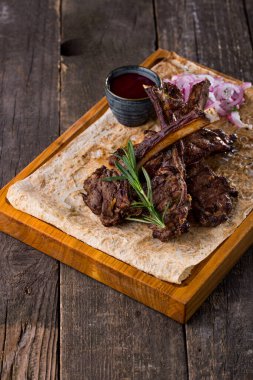 Lamb rack with pickled onions, a sprig of rosemary and cranberry sauce, on pita bread. Food lies on a wooden board. The board stands on a wooden background.