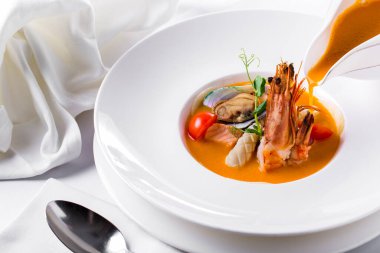 Karidesli Zarzuela çorbası, balık, midye, yeşil bezelye filizi, kaşık ve soslu domates.
