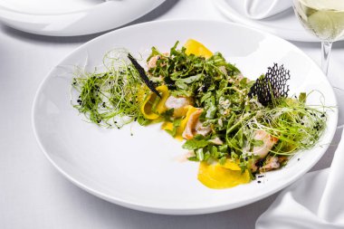 Kalamarlı salata, taze filizler, roka, hindiba, biber, dantel cips, salata ve susam tohumları hafif bir arka planda bir tabakta bir bardak şarapla birlikte.