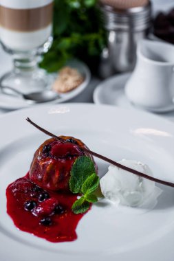 Chocolate dessert with chocolate chunks, blueberries, raspberries, caramel, mint, a scoop of ice cream and a cup of coffee on a white plate. Vertical orientation