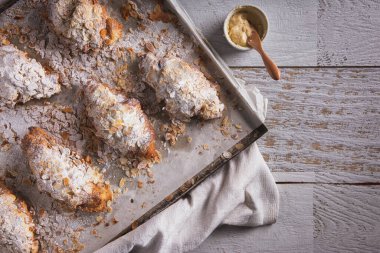 Croissants with condensed milk, powdered sugar and almond slices lying on parchment and a tray with a towel and filling in a bowl.