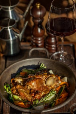 Kemiğin üzerine kızarmış et, biberiye, havuç, soğan, yuvarlak tabakta ıspanak ve bir bardak kırmızı şarap. Dikey yönelim