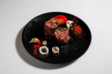 Fried pieces of pork with peppercorns, tomatoes, paprika, salt, thyme, onions and garlic in a plate on a white background