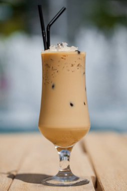 Buzlu, dondurmalı bir kokteyl ve yeşil muz arka planına karşı tahta bir masada duran bir pipet.