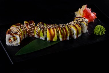 Rolls with eel, sesame seeds, nori, avocado, sauce and Philadelphia cheese in a plate with wasabi and pickled ginger on a black background