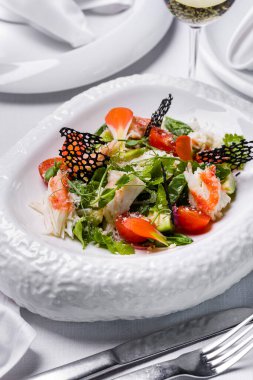 Yengeç salatası, bezelye filizi, domates, marul, dantel cipsi, maydanoz ve peynir hafif bir arka planda bir tabakta bir bardak şarap ve çatal bıçakla birlikte.