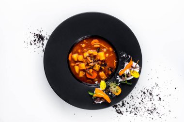 Soup with carrots, mung bean salad, sprouts, flower petals, kumquat, sauce, beans, potatoes and peppers in a plate on a white background