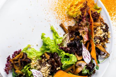 Salad with walnut pieces, dried apples, mushrooms, lettuce, green pea sprouts, flower petals and curry seasoning in a plate on a white background
