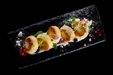 Ekşi kremalı, naneli, mikro yeşil, böğürtlenli, ahududulu ve yenilebilir yapraklı peynirli kekler. Siyah bir levhada yatıyorlar. Siyah bir arkaplanda.