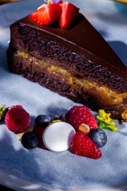 Piece of cake with strawberries, raspberries, blueberries, meringues, jam and chocolate in a plate