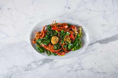 Ispanak ve mısırla süslenmiş, tereyağı ve sarımsak ile kızartılmış haşlanmış kerevit. Yiyecekler dikdörtgen, beyaz bir levhada ve mermer bir yüzeyde duruyor..