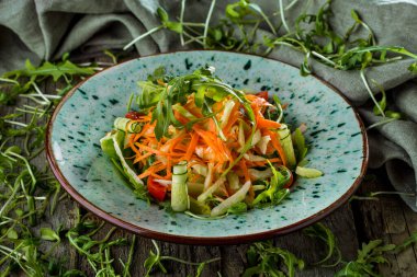 Domatesli salata, roka, biber, havuç, ahşap bir masada salatalık, arkaplanda da mung fasulyesi salatası ve roka.