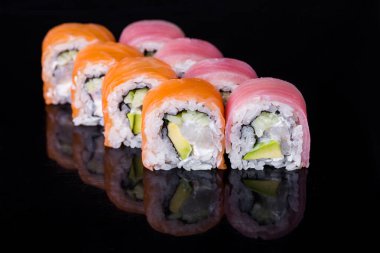 Roll with salmon, tuna, scallops, cucumber, rice, nori and Philadelphia cheese on a black mirror background