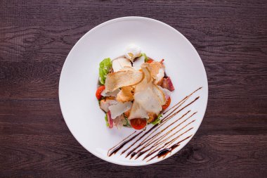 Salad with meat, bacon, tomatoes, cheese and bread in a plate on a wooden background
