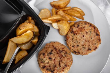 Selyansk-style fried potatoes with fried cutlet in a plate with a spoon and a black plastic container
