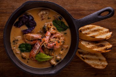 Karides çorbası, fesleğen, salata, roka, kızarmış ekmek ve ahşap bir masa.