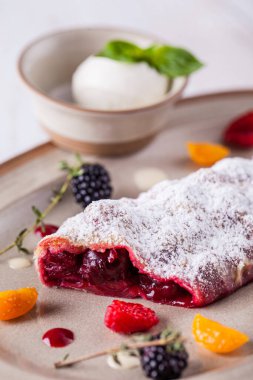Kirazlı çörek ve kısa kabuklu hamur işi çarşaflarından krema. Yanında vanilyalı dondurma topu ve vişne reçelli şeffaf cam tencere var. Yemek seramik bir tabakta. Tabak ahşap bir arka planda duruyor..