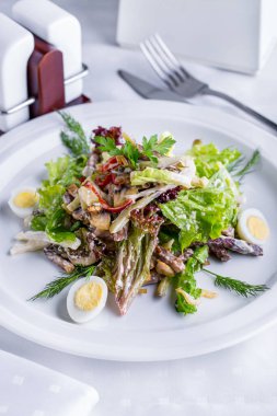 Salad with tomatoes, lettuce, mushrooms, dill, boiled egg in a plate on a light table with cutlery