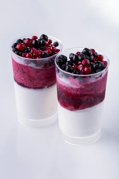 Vanilla ice cream with blueberries and lingonberries in two glasses on a light background. Vertical orientation