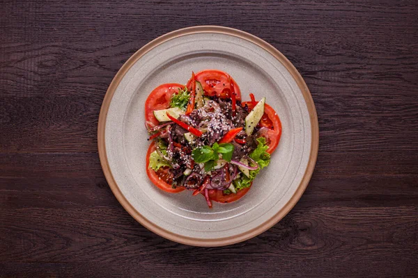 Salad with meat, lettuce, cucumbers, onions, sesame seeds, endive, mint, tomatoes and arugula in a plate on a wooden background