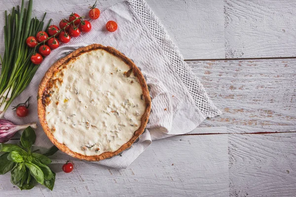 Cheese casserole with tomatoes, basil, garlic, onion and parsley on a towel lying on the table