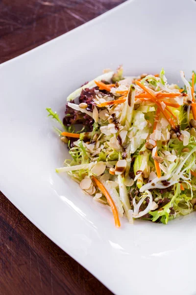 Salad with lettuce, almond slices, wheat, carrots, cucumber, arugula, endive and sauce on a plate on a wooden table