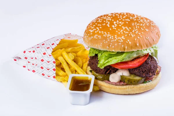 Burger with sesame bun, cutlet, pickled cucumbers, tomatoes, pickled onions, salad with fries and sauce on a white background. Horizontal orientation