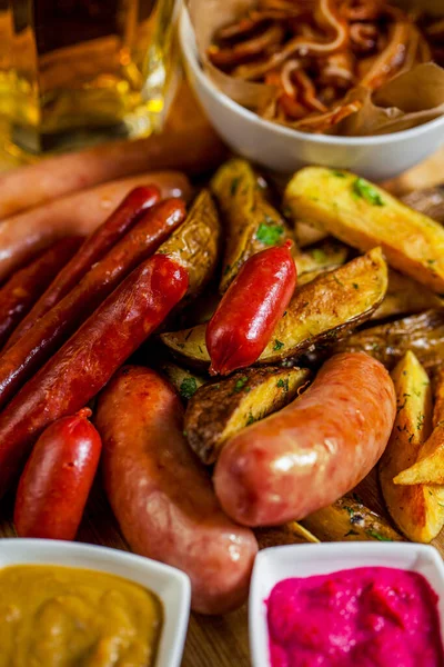 Izgara tavuk, domuz eti, patates kızartmalı tavuk sosisi, peynir, hardal, yabanturpu, ahşap tahtada kişniş ve bir bardak bira..